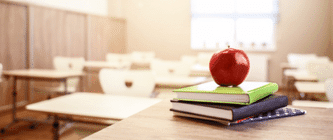 Books and an apple on a desk in a school classroom