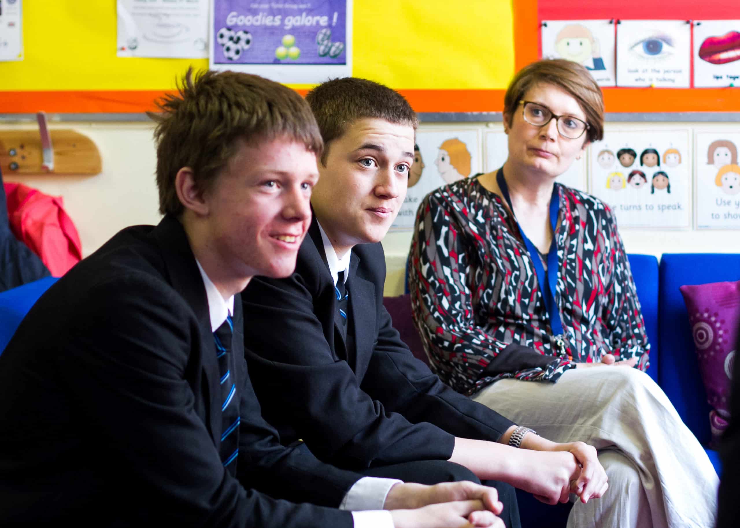 A staff member sitting next to two boys at school