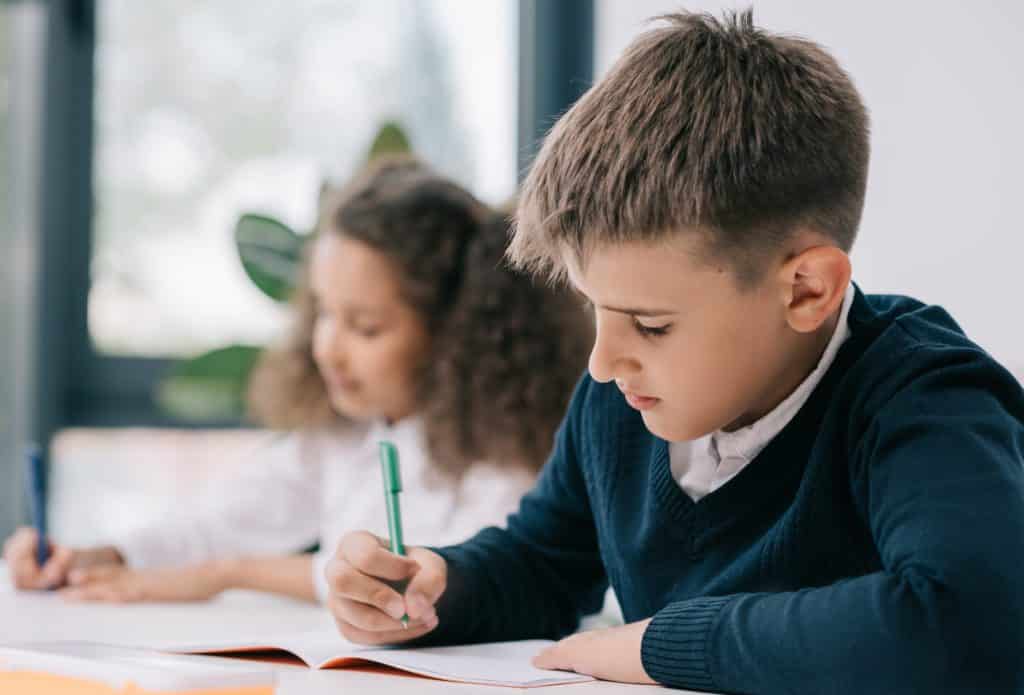A boy and a girl writing on paper at school