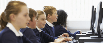 Five school children sitting together whilst looking at computer screens