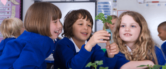 Three school children sitting together looking at a plant