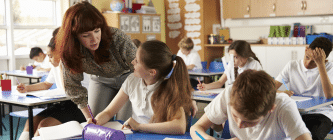 A female teacher talking to a pupil in a classroom with other pupils in the background