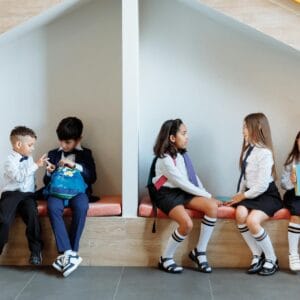 School kids sit on a bench chatting to each other calmly.