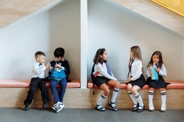 School kids sit on a bench chatting to each other calmly.