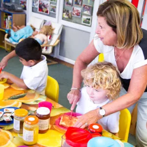 Nurture room pictured with children sitting at a table eating toast. A teacher is helping one child spread their toast.