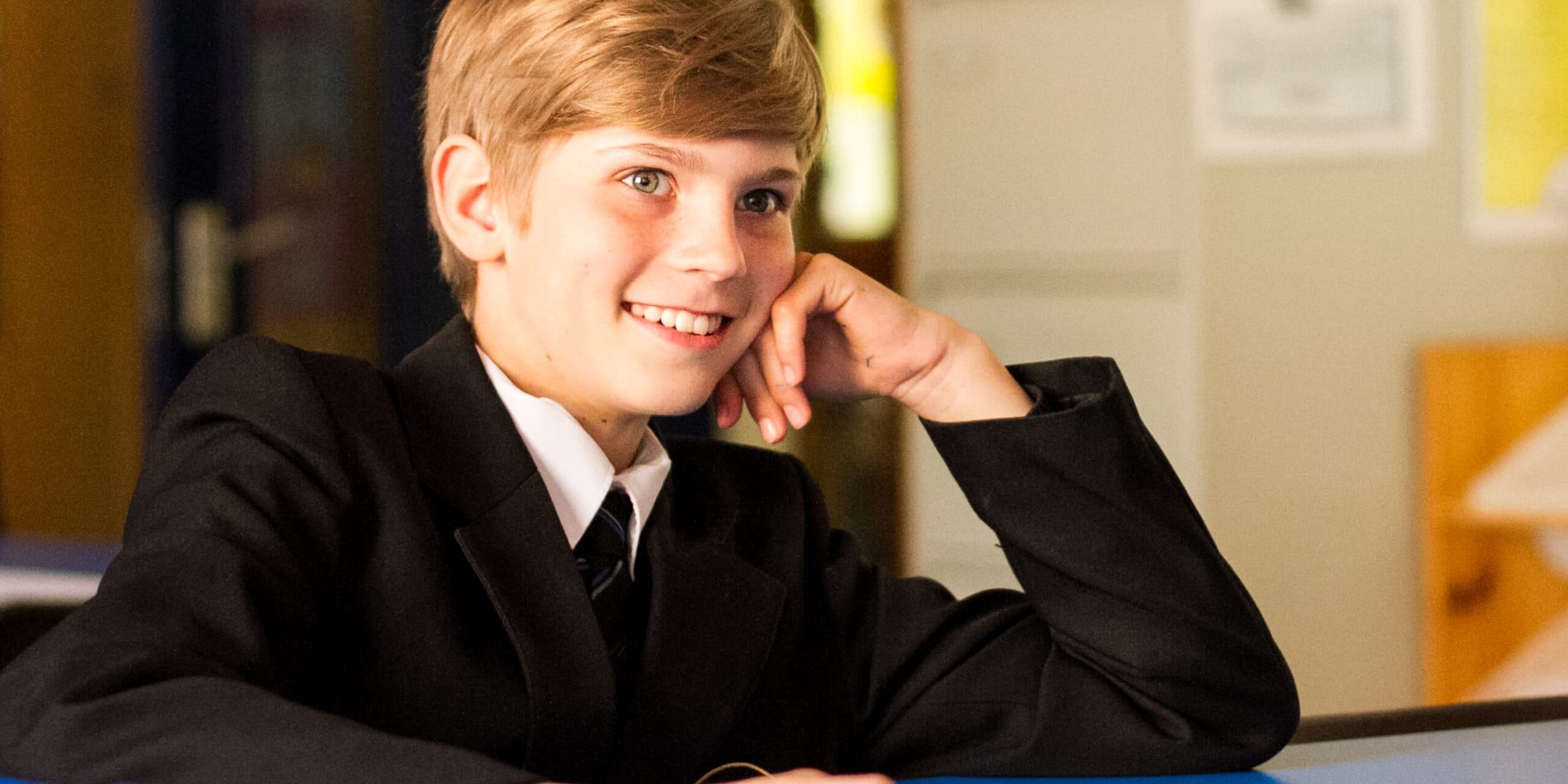 A boy in school uniform sitting at a table and smiling
