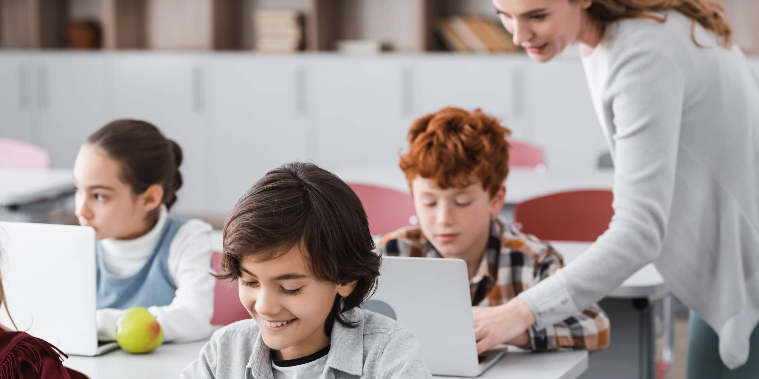 children in school with computers, teacher showing student