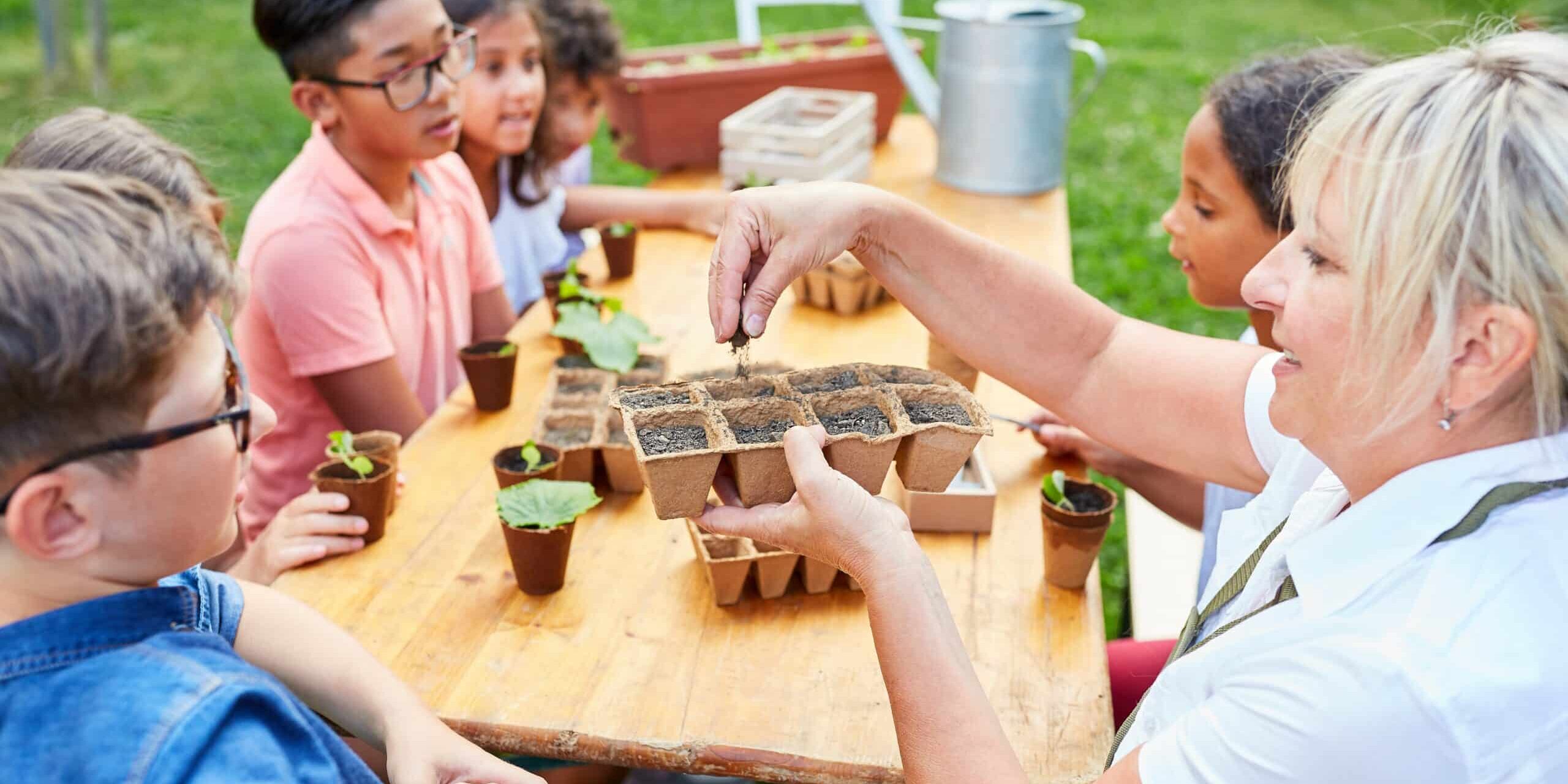 A woman sitting with five children at a table doing gardening activities