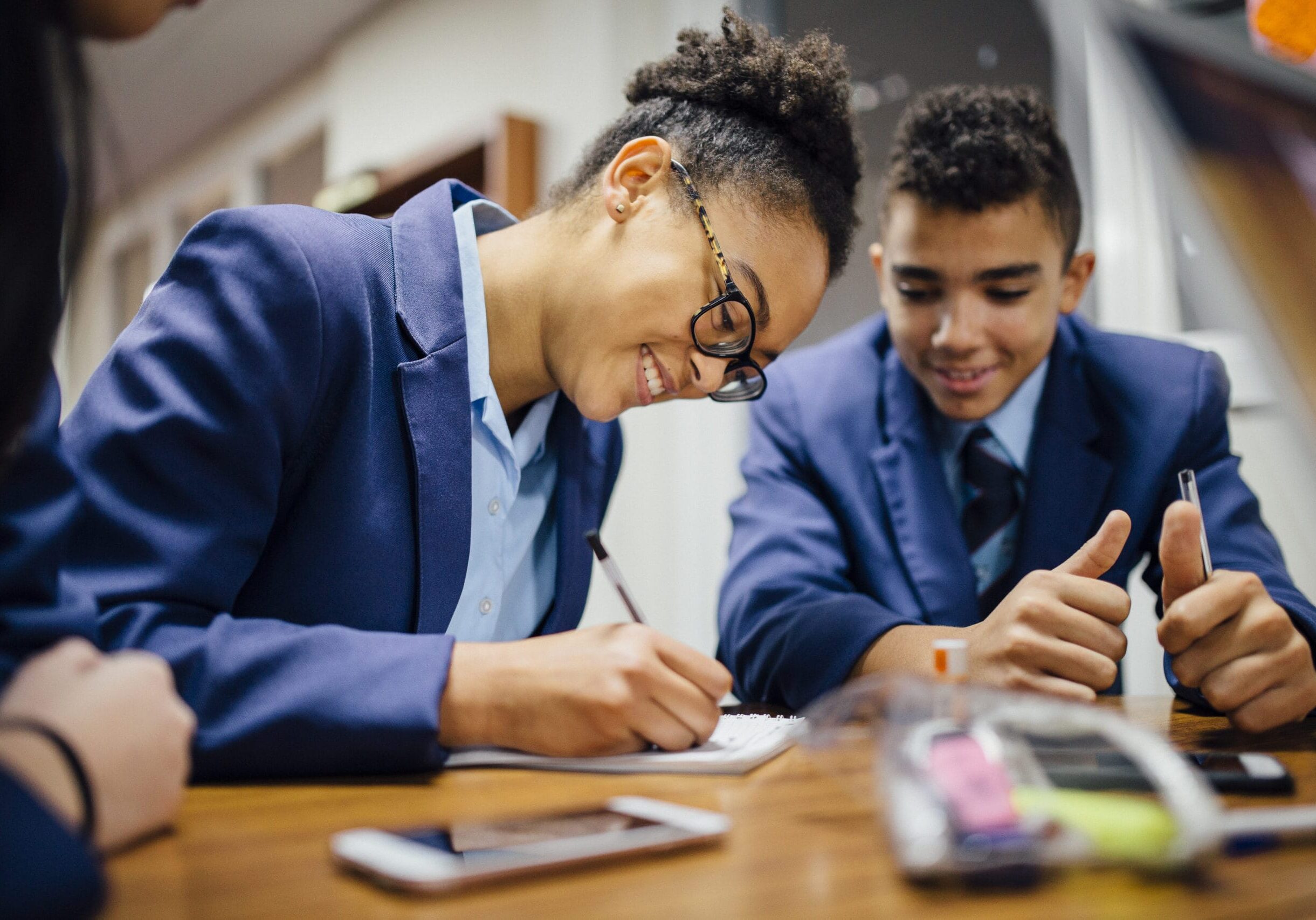 A school girl sitting at a desk writing on paper with a school boy sitting next to her